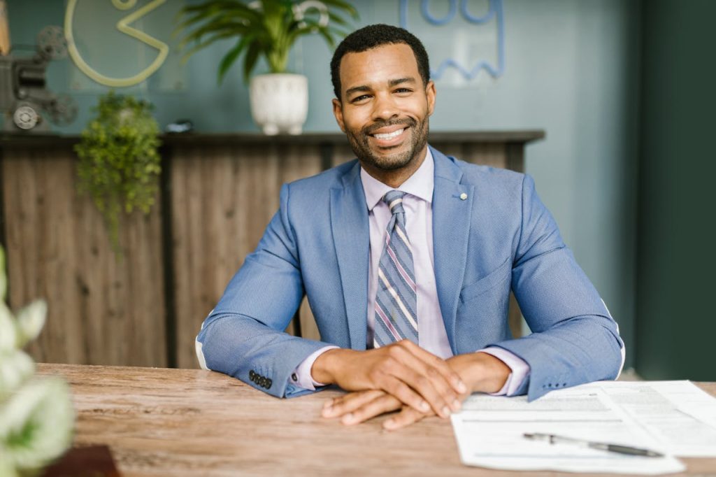 Smiling businessman in office attire sitting at a desk with documents.